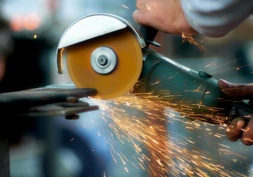 Crop anonymous craftsman using angle grinder to cut metal details while working in workshop